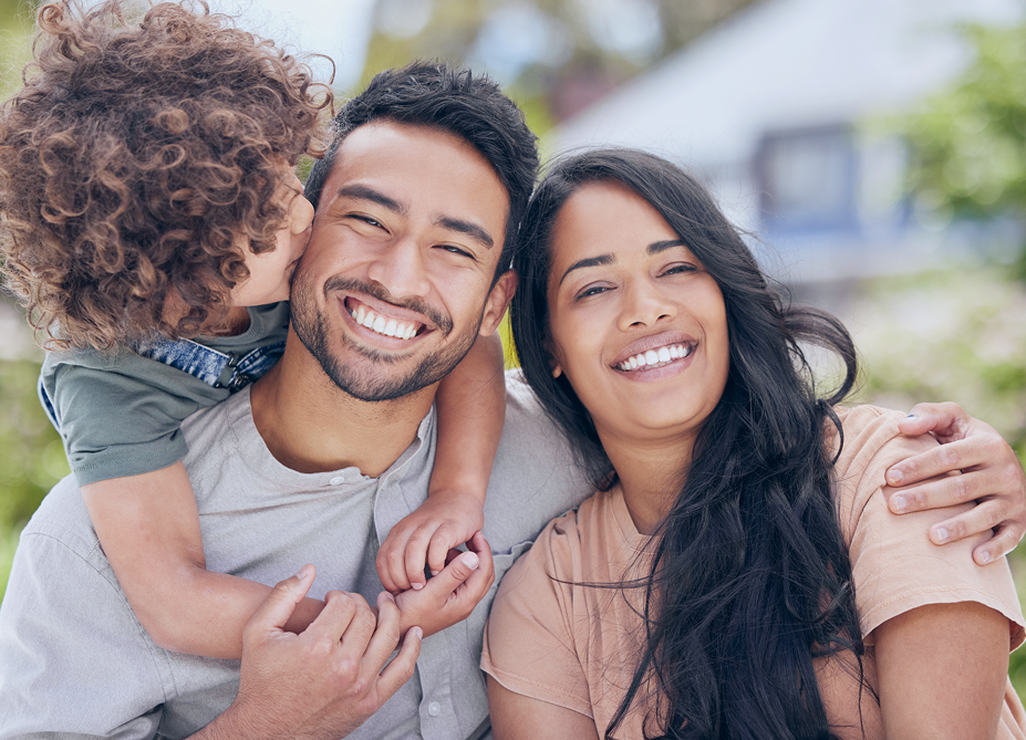 A smiling family of three standing together outside their home.